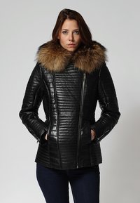 Chaqueta de cuero negra con cuello de piel, textura acolchada y un diseño ajustado. Presenta costura vertical y bolsillos frontales con cremallera.