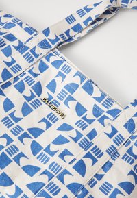 Canvas tote bag featuring a blue wave pattern on a beige background. It has a gold "BILLABONG" logo and sturdy fabric straps.