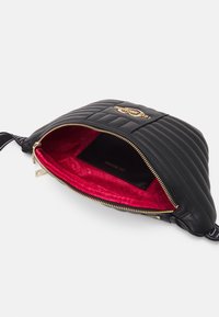 Prošívaná černá kabelka se zlatým logem, s uzavíráním na zip a červeným vzorovaným vnitřkem. Uvnitř obsahuje plochou část na karty.