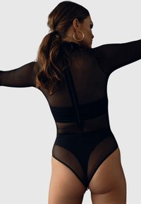 Czarny body z przezroczystymi, długimi rękawami, wysokim dekoltem i krojem string. Zauważalny design pleców z centralnym suwakiem.