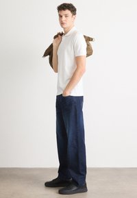 Hvit polo skjorte med korte ermer, sammen med mørkeblå vide jeans. Personen holder en brun lerretsveske over skulderen.
