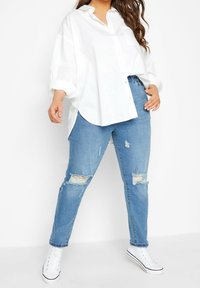 Vit överdimensionerad skjorta med krage och uppvikt ärm, i kombination med ljusblå slitna jeans och vita högstövel sneakers.