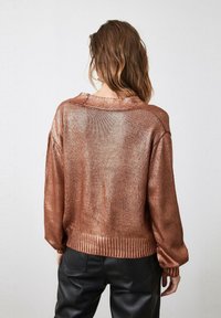 Suéter metálico de cobre con un corte holgado, puños y dobladillo acanalados, y un cuello redondo. Textura suave, mangas largas y un diseño casual.