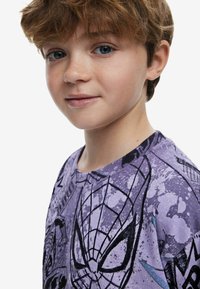 Purple graphic T-shirt featuring a Spiderman design with black outlines and splatter patterns. Soft cotton material with a round neckline.