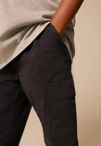 Schwarze Cargo-Hosen mit Seitentaschen, aus einem glatten Material. Das Design zeichnet sich durch eine lockere Passform und einen minimalistischen Stil aus.