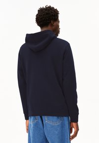 Navyblauer Hoodie mit Kordelzugkapuze, gerippten Bündchen und bequemer Passform. Der Stoff wirkt weich mit einer strukturierten Oberfläche.