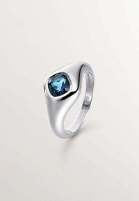 Anillo de plata con un diseño suave y curvado, y una prominente piedra azul engastada en un bisel texturizado. La superficie reflectante realza el color de la gema.