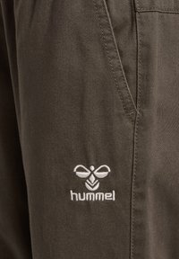 Donkergroene katoenen broek met een gladde textuur, voorzien van een wit geborduurd logo aan de voorkant. Inclusief een detail met een zijzak.