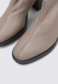 Beige Leder-Ankle Boots mit quadratischer Spitze, die eine genähte Verzierung an der Seite und einen schwarzen Blockabsatz für zusätzliche Stabilität aufweisen.