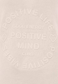 Pull léger beige avec du texte en relief, présentant des phrases comme "VIE POSITIVE" et "BONNE ÉNERGIE", créant un design subtil et texturé.