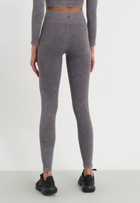 Leggings grigio a coste con vita alta e motivo testurizzato. Abbinati a scarpe da ginnastica nere, la vista mostra un'angolazione posteriore.