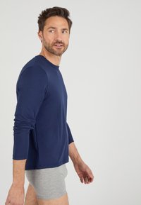 Maglietta a maniche lunghe di colore navy realizzata in un tessuto morbido con scollo rotondo. Sotto vengono indossati boxer grigi. Design semplice, aderente, con dettagli minimi.