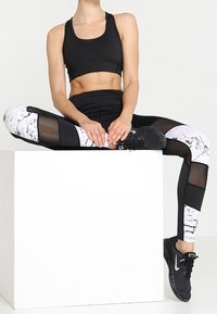 Reggiseno sportivo nero e leggings a vita alta con pannelli in marmo e rete. Presenta un design aderente e tessuto traspirante. Scarpe da ginnastica nere.