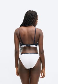 Biele bavlnené spodné prádlo s námorníckomodrými detailmi. Podprsenka má tenké ramienka a zapínanie na háčik a očko; nohavičky majú pás s logom značky.