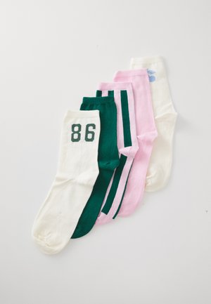 Fünf Paare gefalteter Crew-Socken in Weiß mit "86", einfarbig grün, rosa mit grünen Streifen, einfarbig rosa und weiß mit blauem Logo, auf weißem Hintergrund.