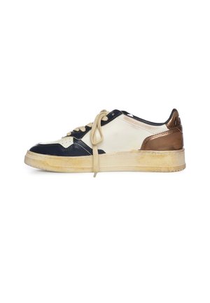 Zapatilla deportiva con paneles beige, negro y bronce, cordones beige y una suela de goma ligeramente desgastada, vista de lado sobre un fondo blanco.