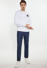 Hvid sweatshirt med logo-detalje, blå denim jeans og hvide sneakers. Outfittet har et afslappet design og en løs pasform.