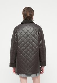 Bruin gewatteerd leren jasje met een brede kraag, geribbelde manchetten en een losse pasvorm, met een gladde textuur en een ruitvormig patroon.