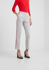 Pantalones ajustados grises con rayas laterales rojas, cintura alta y corte slim. Combinados con zapatos negros de tacón con acentos dorados.