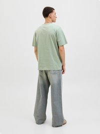 Mėtų žalia trumpomis rankovėmis marškinėliai, pagaminti iš minkštos medžiagos, derinami su laisvais šviesiai džinsiniais džinsais. Paprastas dizainas, be matomų raštų ar logotipų.