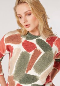 Maglione colorato con un motivo a pennellate in rosso, verde e beige su uno sfondo bianco; scollo e polsini a costine; texture morbida.