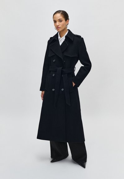 Cappotto trench in lana nera con vita aderente, bottoni doppi, ampi revers e tasche laterali. Texture liscia, design a lunghezza completa.