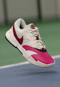 Nike tenisica s gornjim dijelom od bijele mrežice, ružičastim i crvenim akcentima, crnim potplatom, teksturiranim vrhom i istaknutim oznakama na jeziku.
