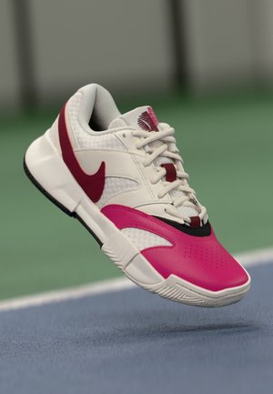 Baskets Nike avec une tige en mesh blanc, des accents roses et rouges, une semelle noire, un bout texturé et un logo bien visible sur la languette.