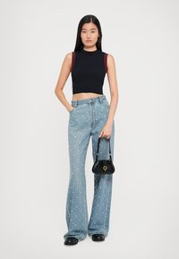Crni rebrasti crop top s bordo akcentima, svijetloplave široke traperice ukrašene bijelim točkicama i mala crna torbica.