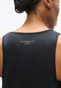 Μαύρο αθλητικό τοπ με απαλή υφή, με στρογγυλή λαιμόκοψη και λογότυπο τυπωμένο στην πλάτη. Απλός, εφαρμοστός σχεδιασμός.