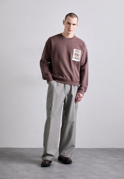 Sweatshirt de algodão castanho com um bolso de remendo à frente, combinado com calças cargo largas em cinza claro, com bolsos laterais e um corte descontraído.