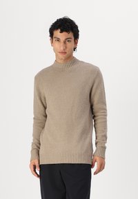 Maglione beige in maglia testurizzata con collo alto e polsini a coste. Design semplice, colore uniforme e vestibilità rilassata sono caratteristiche prominenti.