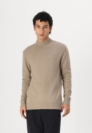 Pulover tricotat texturat, de culoare bej, cu guler înalt și mansete cu nervuri. Design simplu, culoare uniformă și croială lejeră sunt caracteristici proeminente.