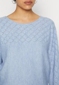 Jasnoniebieski sweter z teksturowanym, diamentowym wzorem na karczku, z okrągłym dekoltem i miękkim, dzianinowym materiałem. Długie rękawy.