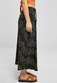 Black wide-leg pants featuring a white floral pattern, elastic waistband, and drawstring. Paired with tan, slip-on, textured sandals.