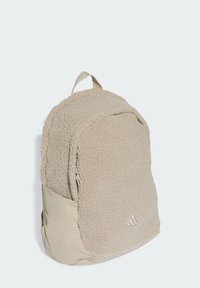 Mochila de forro polar beige con una superficie texturizada. Presenta una sección inferior lisa, un bolsillo con cremallera y un logo en el lateral.
