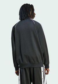 Μαύρο αθλητικό σακάκι με λευκές λεπτομέρειες, χαλαρή εφαρμογή, ραμμένα μανίκια και στρίφωμα. Φοριέται με αντίστοιχα παντελόνια που διαθέτουν κουμπιά snaps και ρίγες.