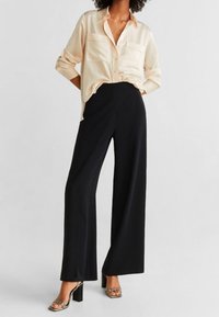 Lys beige, langærmet skjorte med knapper og to brystlommer; parret med høj talje, sorte wide-leg bukser og sølvfarvede hæle sandals.