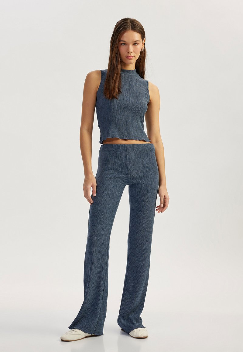 Conjunto de dos piezas en tejido texturizado de color azul oscuro. Top corto sin mangas con dobladillo en forma de ola, combinado con pantalones ajustados y acampanados.