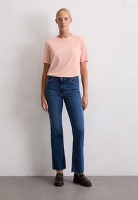 T-shirt à manches courtes rose clair associé à un jean droit bleu foncé. Le jean présente un ourlet brut et une fermeture à bouton classique.