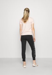 Ljusrosa t-shirt med kort ärm, ihop med svarta joggingsbyxor med tryckta sidodetaljer, avsmalnande muddar och avslappnade skor.