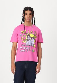 Pink cotton t-shirt featuring a graphic print with names, flowers, and peace symbols. Short sleeves and a relaxed fit.