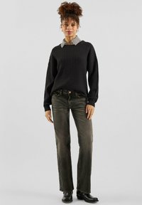 Czarny sweter o fakturze, nałożony na szarą koszulę w kratę, zestawiony z ciemnoszarymi jeansami o prostych nogawkach i czarnymi botkami za kostkę.