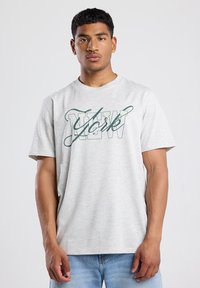 Grijze t-shirt met korte mouwen en een ronde halslijn, met een donkergroene "New York" grafiek over de borst. Soepele stofstructuur.