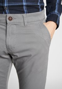 Graue, taillierte Hose mit Knopfverschluss und seitlichen Taschen. Hergestellt aus einem glatten Stoff mit dezenten Nähdetails und klassischem Schnitt.