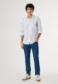 Lys blåstripete langermet skjorte, blå jeans og hvite joggesko med grå detaljer. Avslappet passform, knappedown krage og rullede ermer.