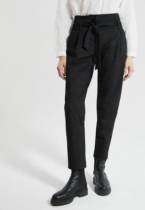 Zwarte, taillehoge broek met een strikceintuur, gemaakt van een gestructureerde stof en voorzien van een taps toelopend ontwerp. Draagt bijpassende zwarte enkellaarsjes.