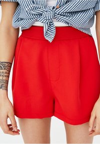Shorts rouges taille haute avec une coupe ajustée et une texture lisse, présentant une couture frontale et des poches latérales.