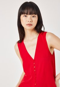 Red sleeveless top with a deep V-neck and a row of buttons down the front. Material appears lightweight with a subtle texture.