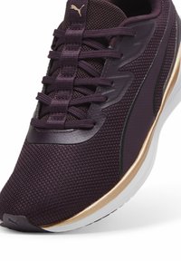 Zapatilla deportiva morada con parte superior de malla, acentuada por una franja dorada, cordones planos y una suela blanca acolchada para mayor comodidad y estabilidad.